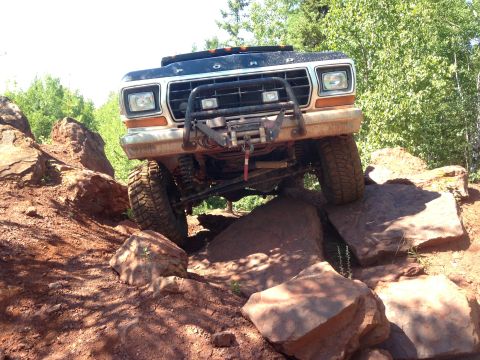 1979 Ford Bronco - A black 1979 Ford Bronco is navigating a rocky, off-road trail with large boulders. The front of the vehicle is angled towards the viewer,…
