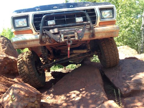 1979 Ford Bronco - A lifted 1979 Ford Bronco is shown navigating a rocky obstacle course, with its front tire high on a large boulder. The vehicle features a…
