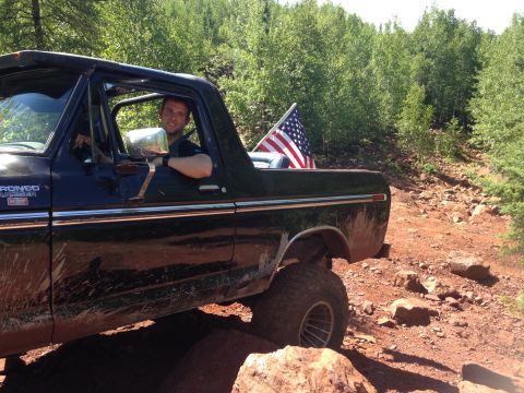 1979 Ford Bronco - A man is driving a black Ford Bronco Ranger off-road on a rocky, dirt path surrounded by trees. An American flag is visible in the truck be…
