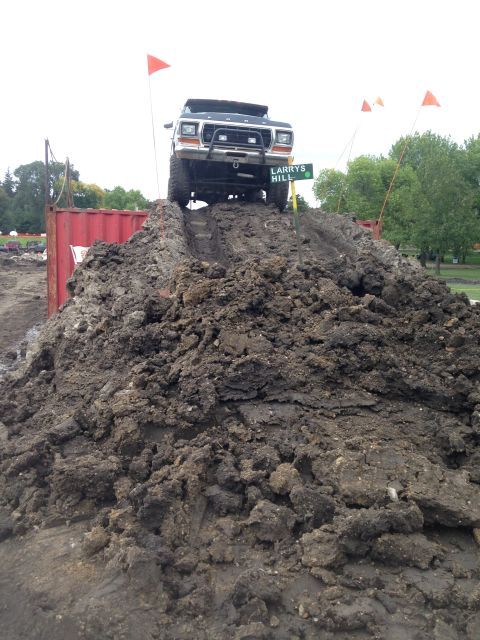 1979 Ford Bronco - A black 1979 Ford Bronco is positioned at the top of a large mud hill, with orange flags marking the course. The vehicle is facing forward,…