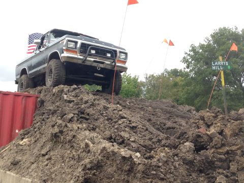 1979 Ford Bronco - A black 1979 Ford Bronco is positioned on a large dirt mound, with an American flag attached to the driver's side rear. Orange flags and a…