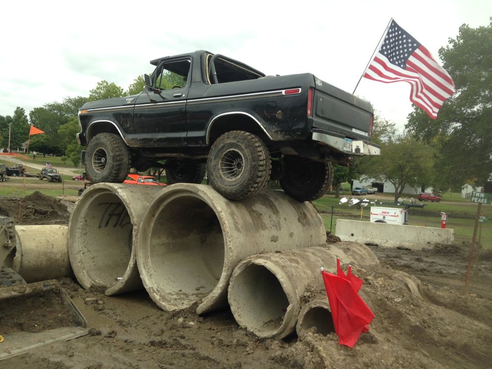 Black 1979 Ford Bronco on concrete pipes with American flag.
