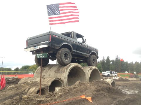 1979 Ford Bronco - A black Ford pickup truck with an American flag mounted on a pole is positioned on top of large concrete pipes. A sign reading "TWIN PEAKS"…