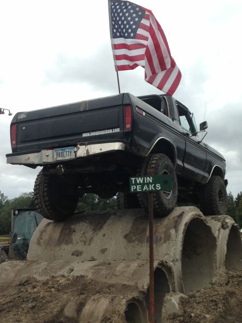1979 Ford Bronco - A black 1970s era Ford pickup truck, modified for off-road use, is parked on top of large concrete culverts. An American flag is mounted on…