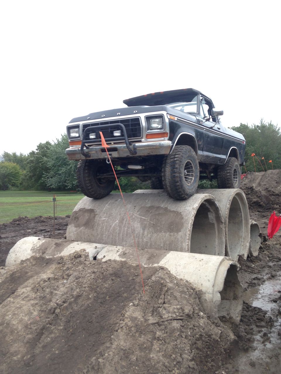 1979 Ford Bronco with bull bar and off-road tires driving over concrete pipes on a dirt course