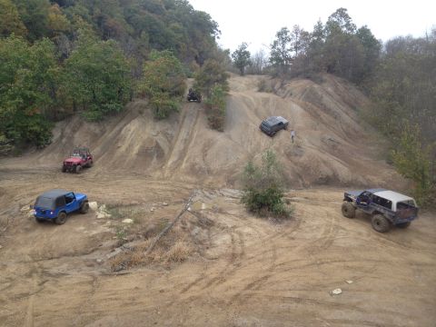 1979 Ford Bronco - Multiple off-road vehicles are seen traversing a challenging dirt terrain on a cloudy day.