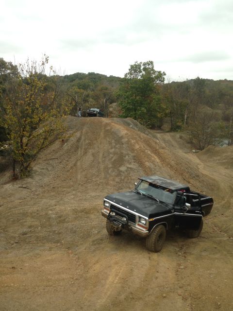 1979 Ford Bronco - A black 1980s Ford F-Series truck is seen off-roading on a dirt hill with another vehicle in the distance.