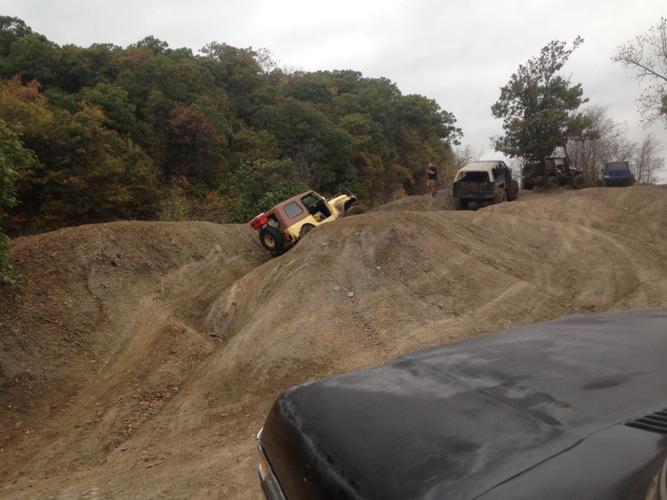 Off-road vehicles navigating a steep dirt hill, one yellow and brown Jeep is tilted on its side