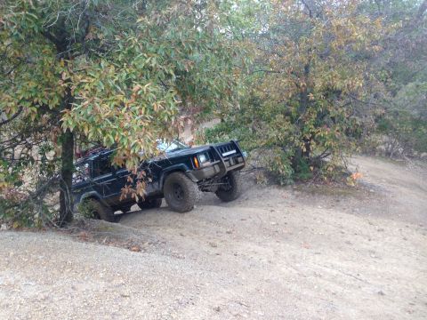 1979 Ford Bronco - A black Jeep Cherokee XJ navigates a steep, wooded trail.