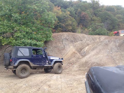 1979 Ford Bronco - Jeep Wrangler navigating an off-road trail with wooded hills in the background.
