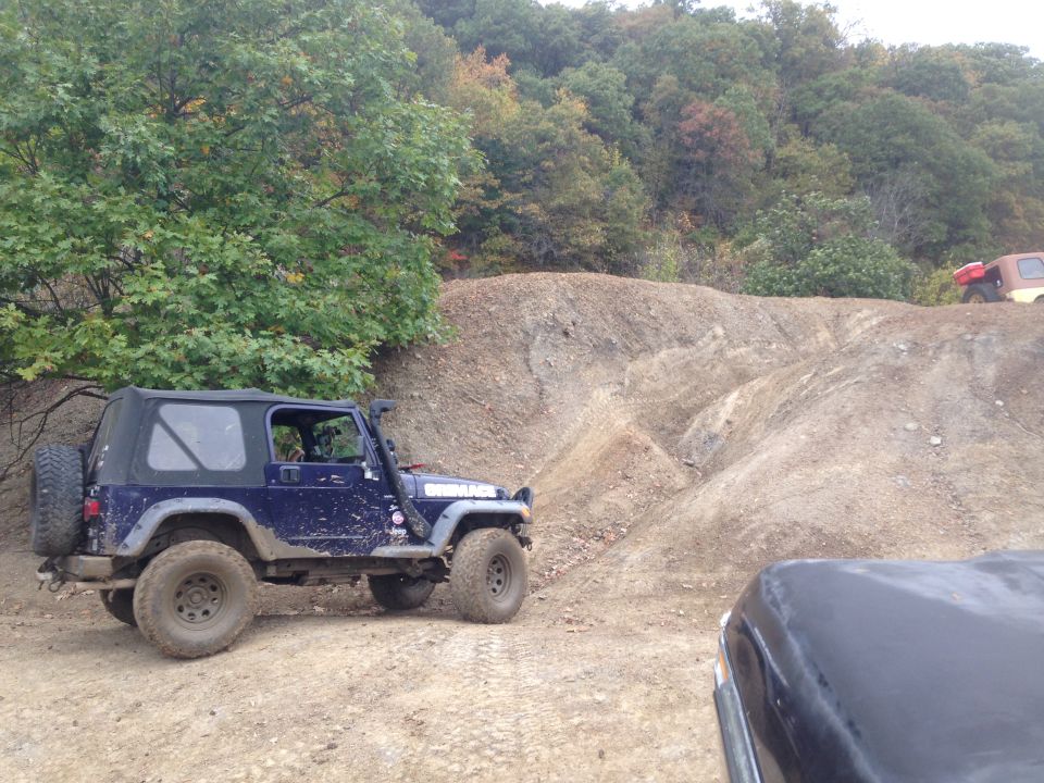 Blue Jeep Wrangler with soft top on a dirt trail, another vehicle in foreground