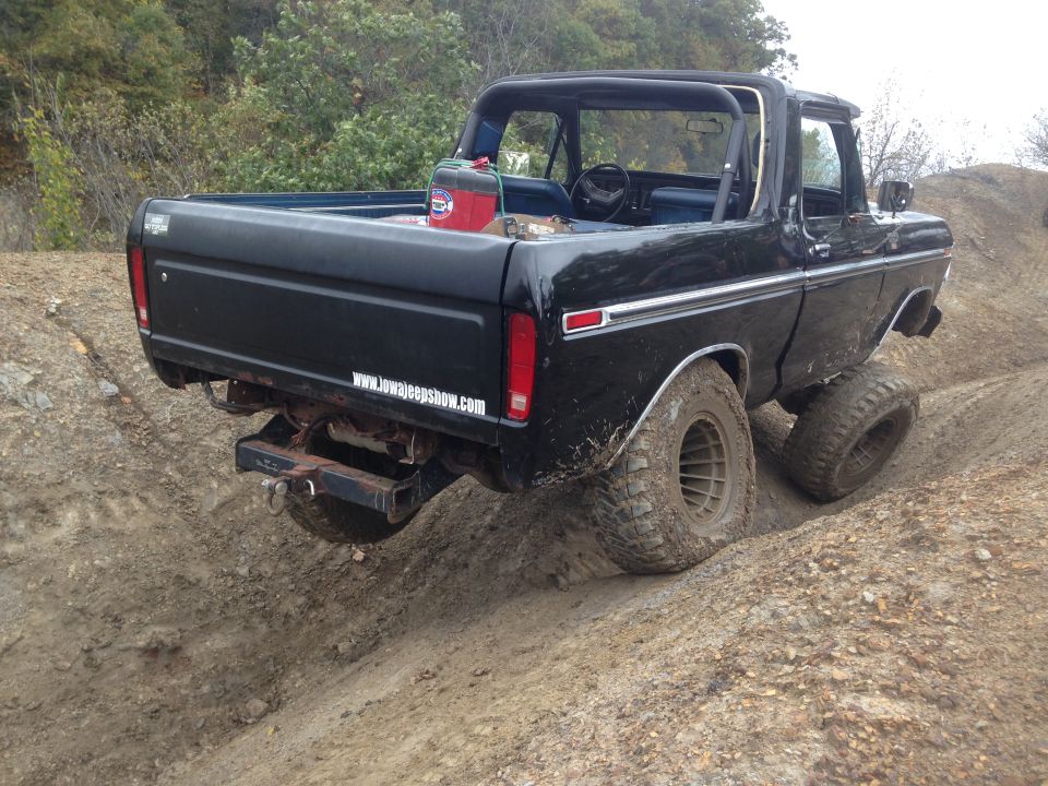 Black Ford Bronco with roll cage on a dirt trail, rear view. www.iowajeepshow.com sticker on tailgate