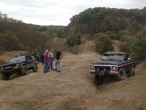 1979 Ford Bronco - A group of people stand near a black 1979 Ford Bronco and a dark SUV on a dusty off-road trail.