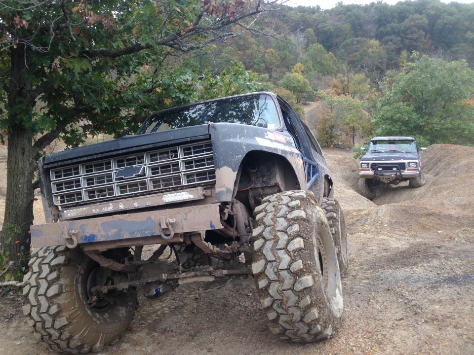 Muddy off-road SUV with large tires and a Chevrolet grille, another SUV behind it