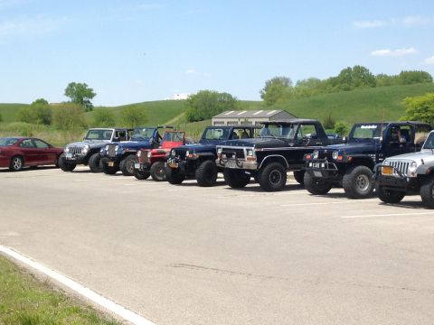 1979 Ford Bronco - A collection of off-road vehicles, including a black Ford truck and several Jeeps, are parked in a lot on a sunny day.