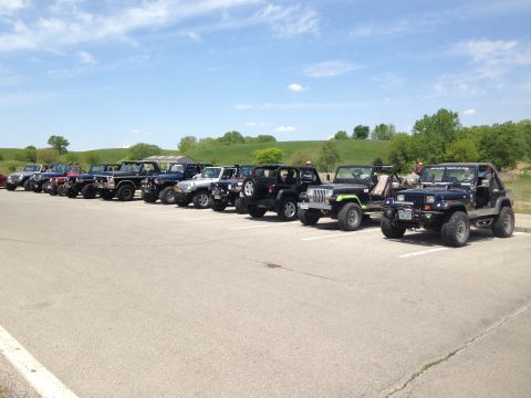1979 Ford Bronco - A group of Jeeps are parked in a lot under a blue sky with scattered clouds.