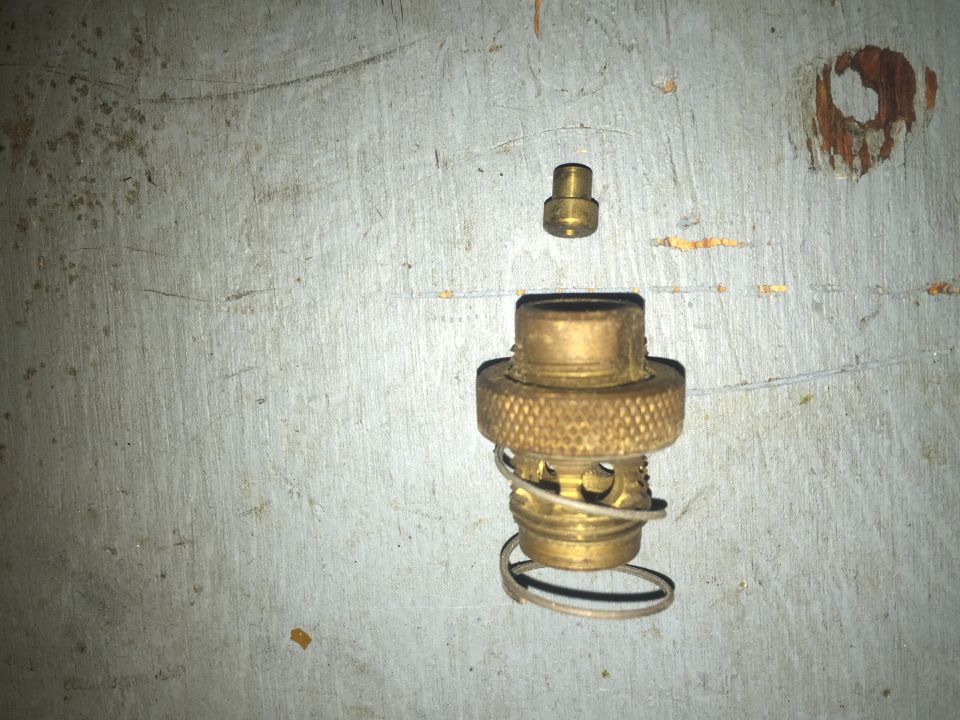 Brass valve assembly with spring and cap on metal surface. Supermotors.net logo visible