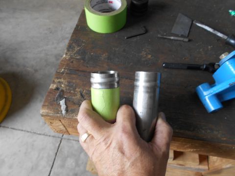 1992 Ford Bronco - A hand holds two metal cylinders, one wrapped in green tape, on a workbench with various tools and a roll of tape.