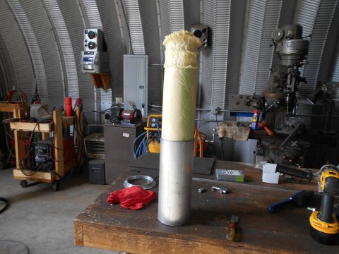 1992 Ford Bronco - An exhaust pipe, partially covered in foam insulation, sits on a workbench in a garage with tools and machinery in the background.