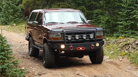 1996 Ford Bronco - This maroon Ford Bronco is shown on a dirt road with trees in the background.