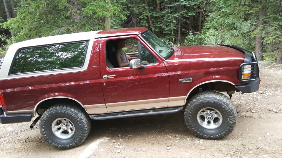 Red 1996 Ford Bronco with white top on dirt road