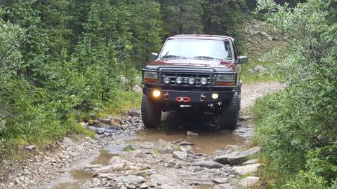 1996 Ford Bronco - A red 1996 Ford Bronco navigates a challenging off-road path with water and rocks.