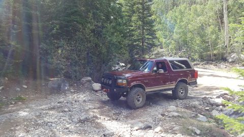 1996 Ford Bronco - 1996 Ford Bronco navigating a rough, rocky path through a wooded mountain area.