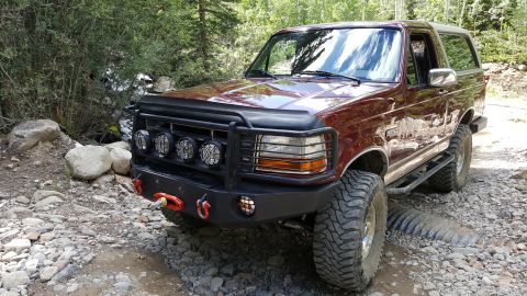 1996 Ford Bronco - This modified Ford Bronco is parked on a rough, rocky path surrounded by trees.