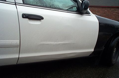 2001 Ford Crown Victoria - This police car has a dent on its white door panel. The rear fender is painted black.