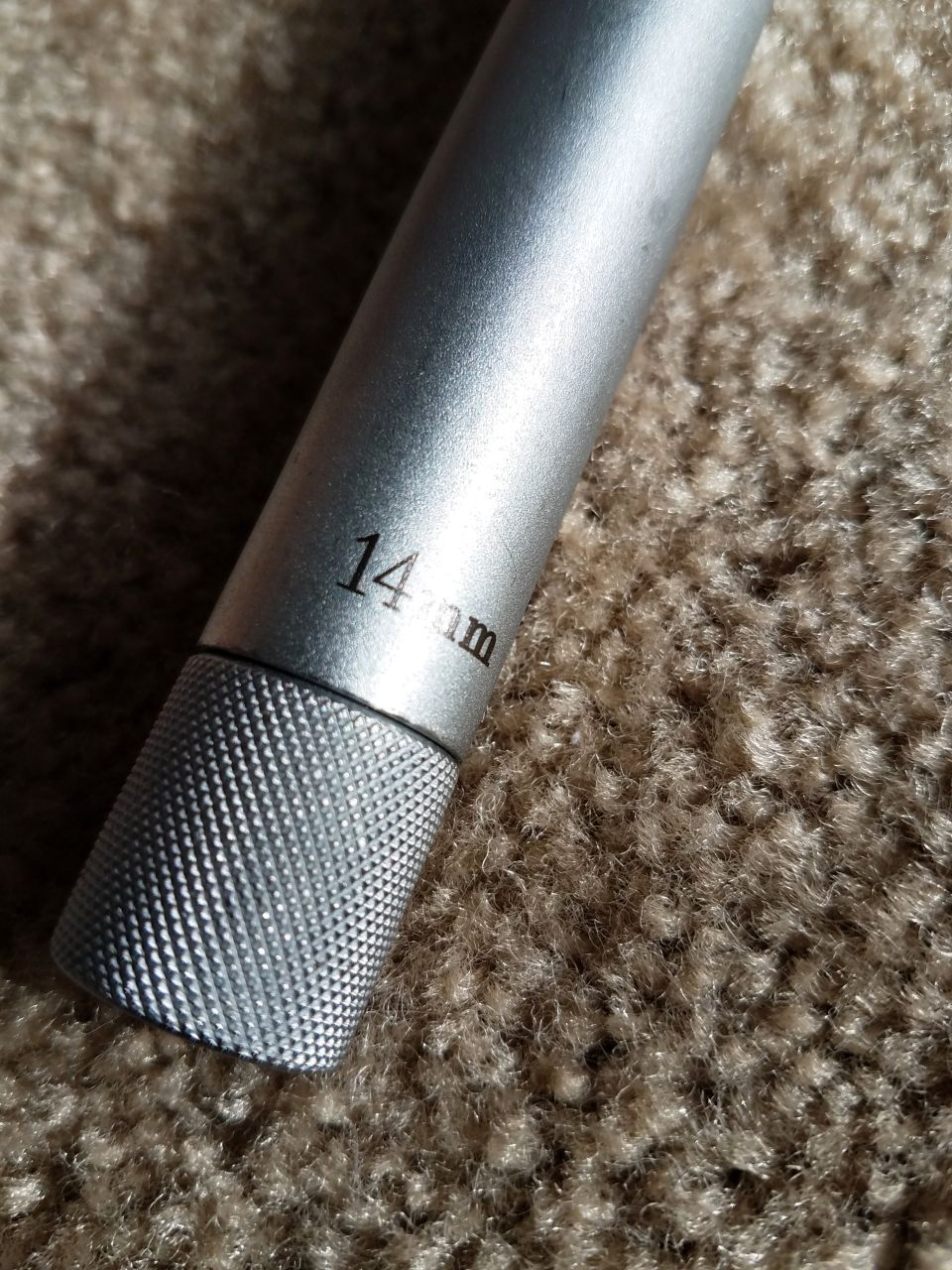 Silver 14mm socket wrench with knurled grip, lying on carpet