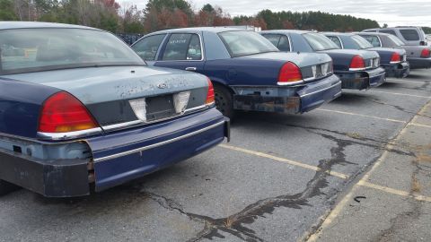 1991 Ford LTD Crown Victoria - Several Ford Crown Victorias are parked in a lot, showing their rear ends. Some have missing bumpers.