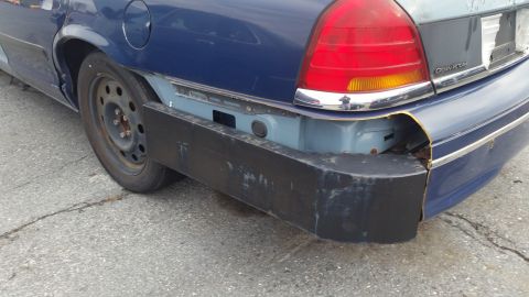 1991 Ford LTD Crown Victoria - Rear view of a blue Ford Crown Victoria with a damaged bumper and visible rust.