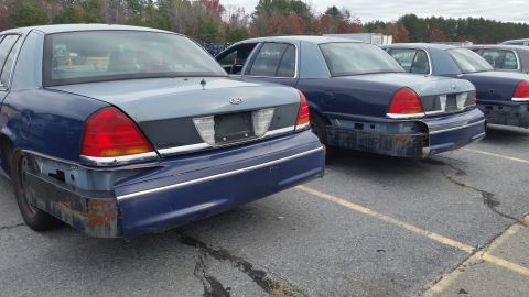 1991 Ford LTD Crown Victoria - Multiple blue Ford Crown Victorias are lined up, all missing their rear bumpers and showing signs of wear.