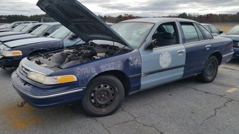 1991 Ford LTD Crown Victoria - A former state police car, a Ford Crown Victoria, sits with its hood open in a lot with other vehicles.