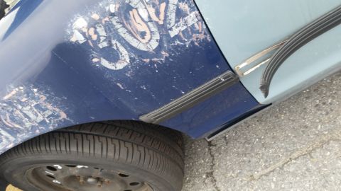 1991 Ford LTD Crown Victoria - Close-up of a car's side showing damaged paint and trim on the fender and door.