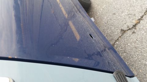 1991 Ford LTD Crown Victoria - A blue car hood with a hole in it, parked on asphalt.