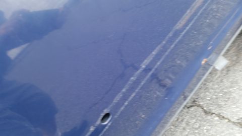 1991 Ford LTD Crown Victoria - A close-up view of a blue car door shows some wear and tear, including cracks and a small hole.