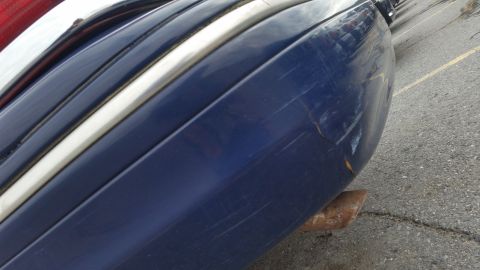 1991 Ford LTD Crown Victoria - Close-up of a damaged blue car bumper with chrome trim and a rusty exhaust pipe.
