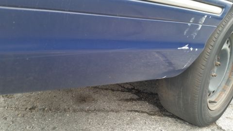 1991 Ford LTD Crown Victoria - Close-up of a blue sedan's side panel showing damage and a deflated tire.
