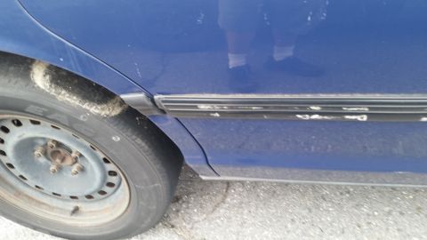1991 Ford LTD Crown Victoria - Close-up view of the side panel and wheel of a blue vehicle, showing wear on the trim.