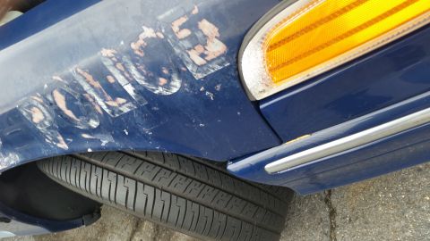 1991 Ford LTD Crown Victoria - Close-up of a blue police car's fender showing weathered 'POLICE' lettering and an amber turn signal light.