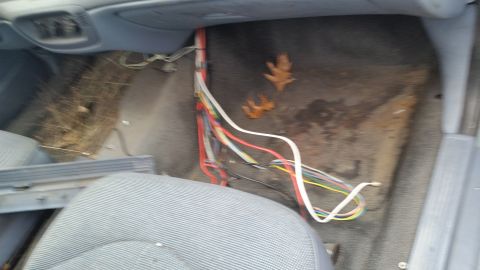 1991 Ford LTD Crown Victoria - The interior floor of a car shows exposed wiring and debris, with fallen leaves scattered on the carpet.