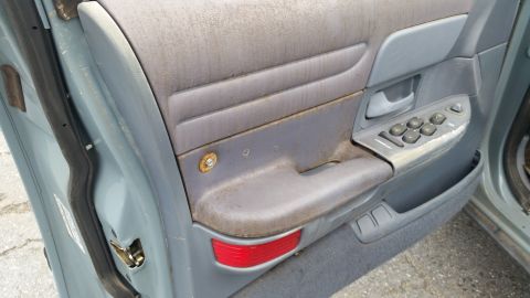 1991 Ford LTD Crown Victoria - Close-up of a car's interior door panel, revealing worn window controls and a dusty armrest.