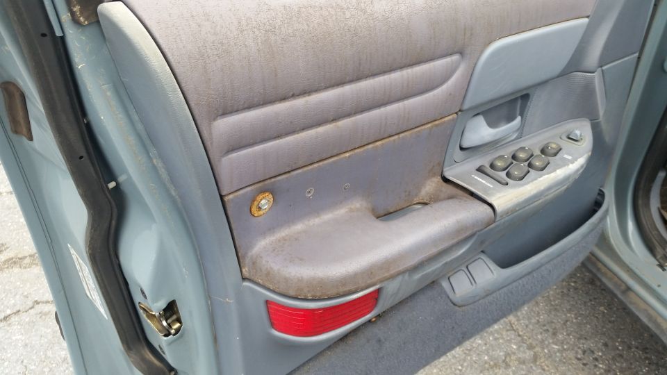 Interior of a car door, showing the armrest, window controls, and door panel. It looks dirty