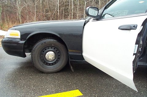 2001 Ford Crown Victoria - The side profile of a black and white 2001 Ford Crown Victoria police car, with the driver's door ajar.