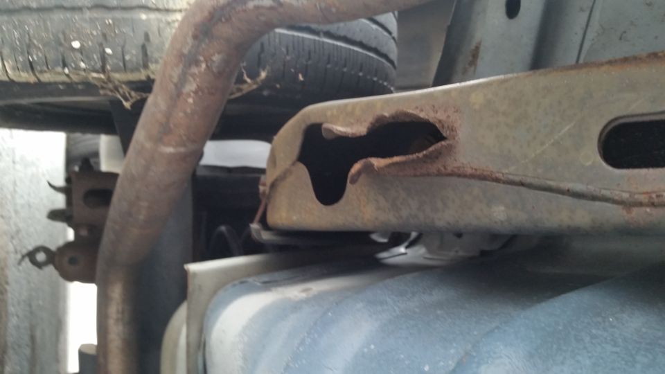 rusted metal frame with a large hole, part of a vehicle's undercarriage, with exhaust pipe and tire visible