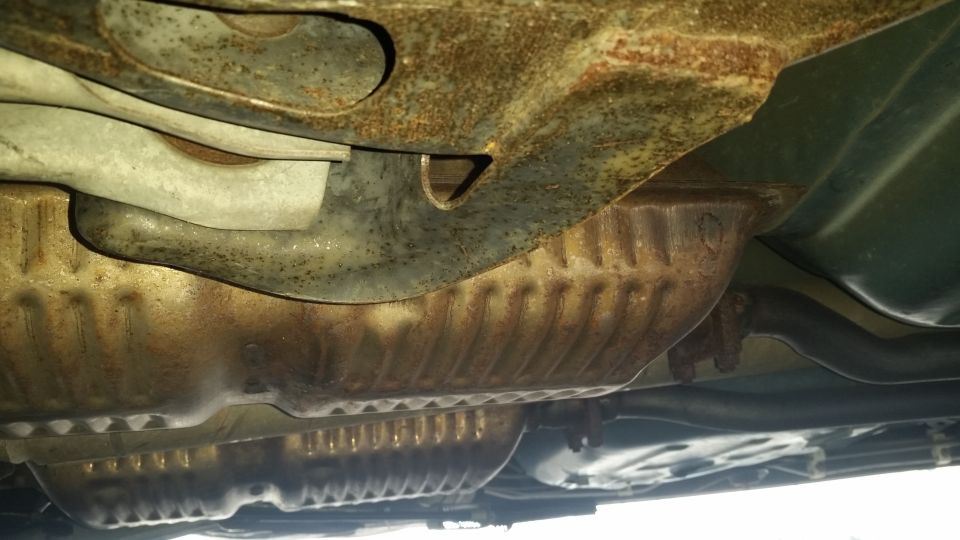 Underside of a vehicle showing rusted exhaust components and frame