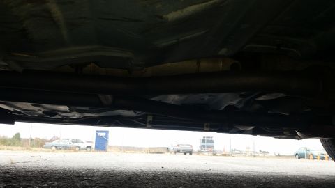 1991 Ford LTD Crown Victoria - The underside of a vehicle is visible, with several other cars and a portable toilet in the distance.