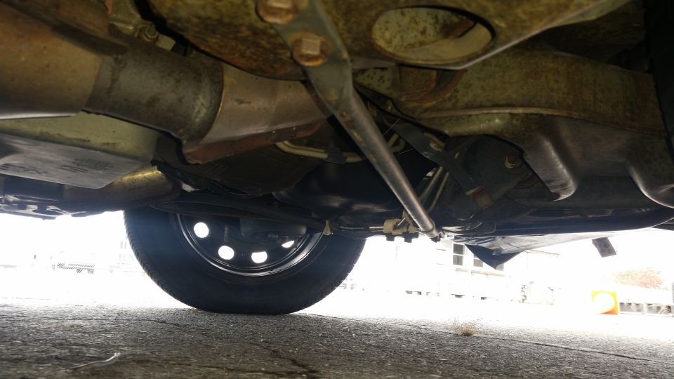 Undercarriage view showing suspension components, exhaust pipe, and a wheel with a hubcap