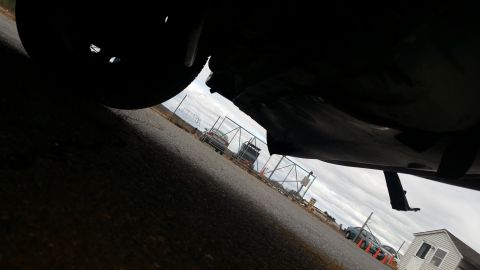 1991 Ford LTD Crown Victoria - The underside of a vehicle is visible, with other cars and a fence in the background under a cloudy sky.